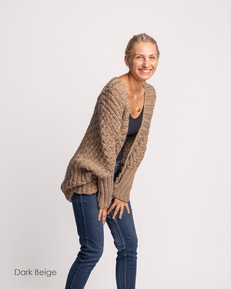 May include: A woman wearing a dark beige knitted cardigan with a relaxed fit and long sleeves. She is also wearing blue jeans.