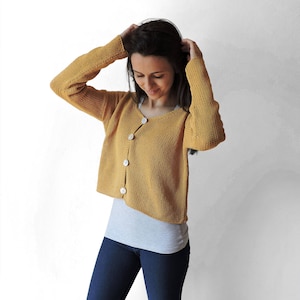 May include: A mustard yellow cardigan with long sleeves and button closure. The cardigan is cropped and has a relaxed fit.
