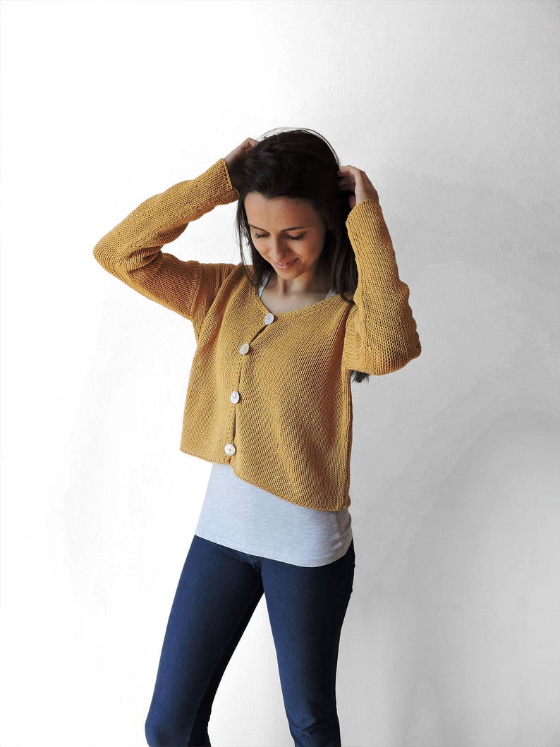 May include: A mustard yellow cardigan with long sleeves and button closure. The cardigan is cropped and has a relaxed fit.