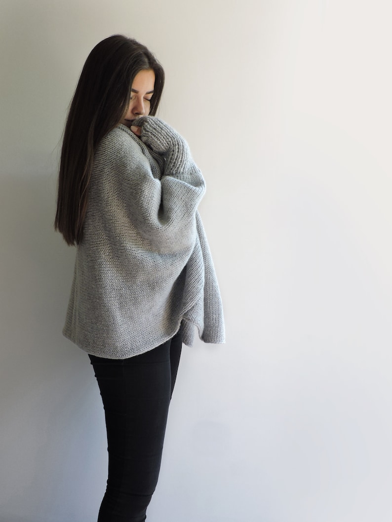 May include: A woman wearing a gray knitted sweater with long sleeves and black pants.
