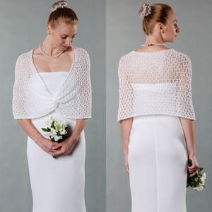 May include: White crochet bridal shrug with a delicate openwork pattern. The shrug is shown on a model wearing a white wedding dress.