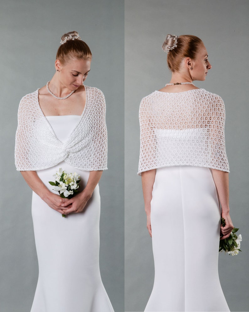 May include: White crochet bridal shrug with a delicate openwork pattern. The shrug is shown on a model wearing a white wedding dress.