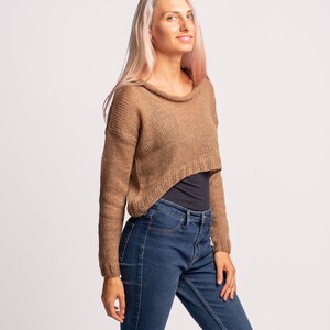 May include: A woman wearing a brown cropped sweater with long sleeves and blue jeans.