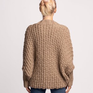 May include: A dark beige knitted cardigan with a relaxed fit and long sleeves. The cardigan is made from a soft, chunky yarn and has a ribbed texture.