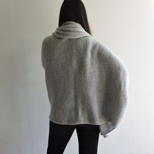 May include: A gray knitted sweater with a cowl neck and long sleeves. The sweater is loose fitting and has a relaxed silhouette.
