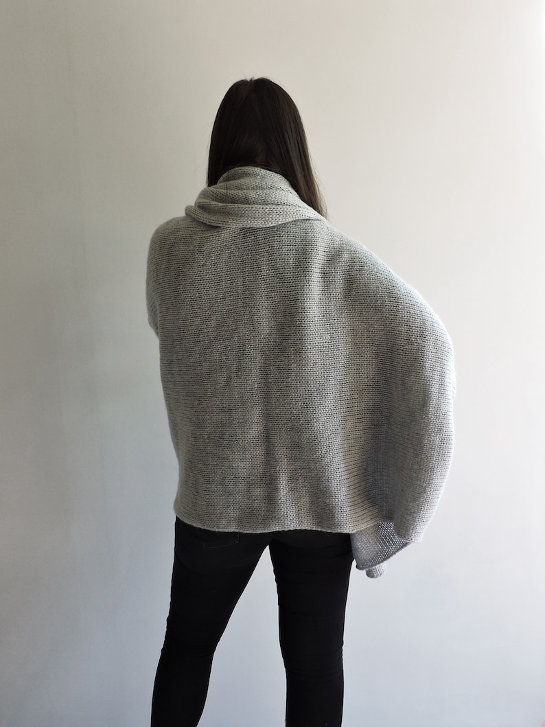 May include: A gray knitted sweater with a cowl neck and long sleeves. The sweater is loose fitting and has a relaxed silhouette.