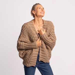 May include: A dark beige knitted cardigan with a relaxed fit and long sleeves. The cardigan is open at the front and has a V-neck.