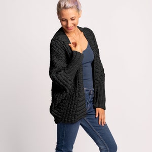 May include: A black knitted cardigan with a relaxed fit and a slightly oversized silhouette. The cardigan is made of a soft, chunky yarn and has a simple, classic design.