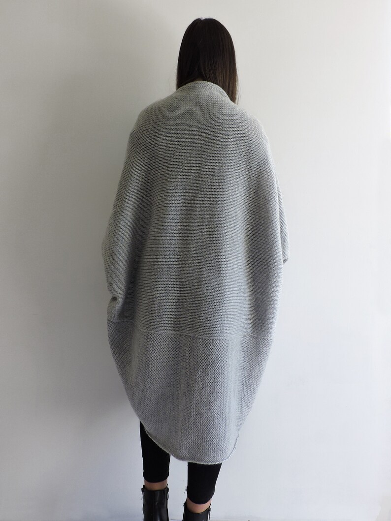 May include: A gray knitted cardigan with a long, loose fit. The cardigan has a ribbed texture and a slightly longer back than front.