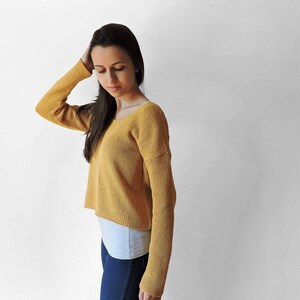 May include: A mustard yellow knitted sweater with long sleeves and a slightly cropped hem.