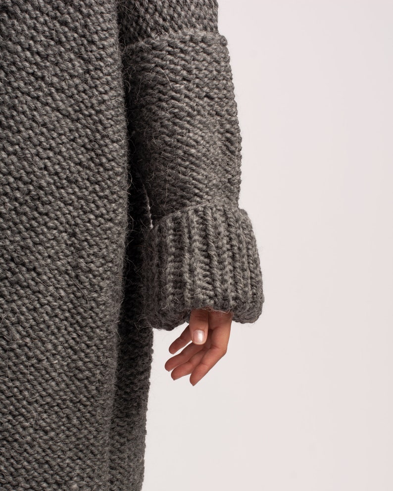 Puede incluir: Un c&aacute;rdigan gris de punto con mangas largas y textura acanalada. El c&aacute;rdigan tiene un corte holgado y un aspecto ligeramente oversized.