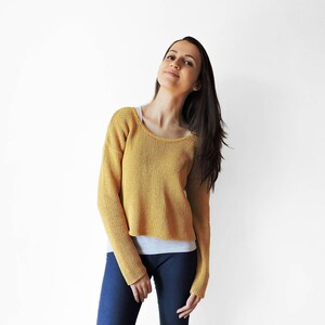 May include: A woman wearing a yellow knitted sweater with long sleeves and blue jeans.