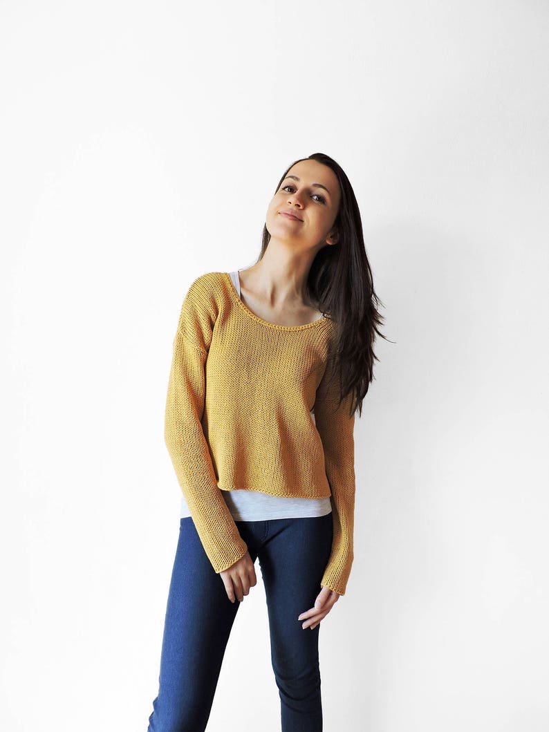 May include: A woman wearing a yellow knitted sweater with long sleeves and blue jeans.