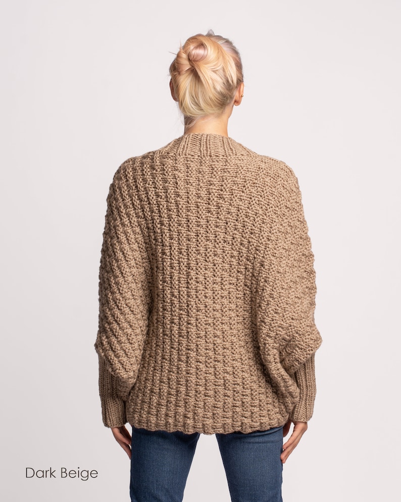 May include: A dark beige knitted cardigan with a relaxed fit and long sleeves. The cardigan is made from a soft, chunky yarn and has a ribbed texture.