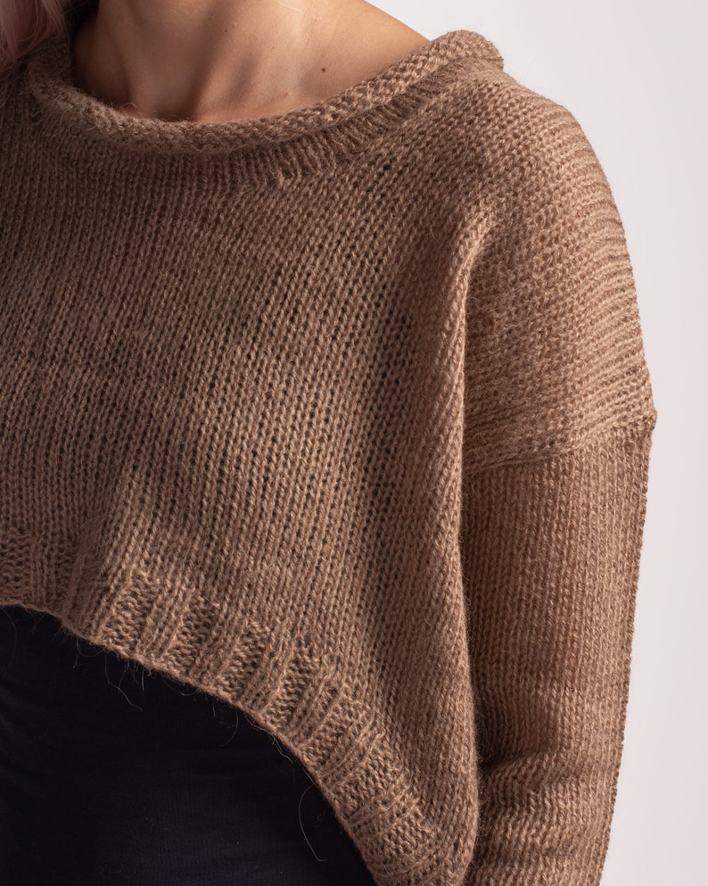 May include: A brown knitted sweater with a cropped hem and long sleeves.