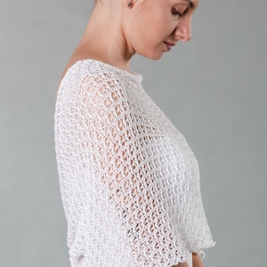 May include: White crochet shrug with a delicate open-weave pattern. The shrug is lightweight and airy, perfect for layering over a dress or top.