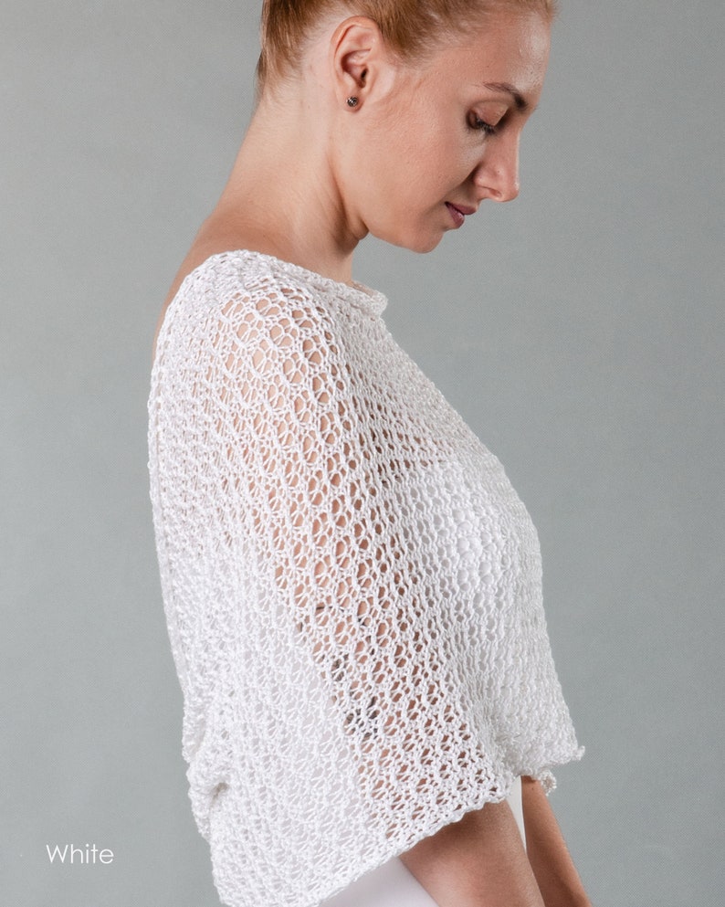 May include: White crochet shrug with a delicate open-weave pattern. The shrug is lightweight and airy, perfect for layering over a dress or top.