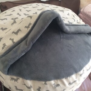 May include: A gray and white dog bed with a removable, gray fleece cover. The bed has a  pattern of small, black dachshund silhouettes on a white background.