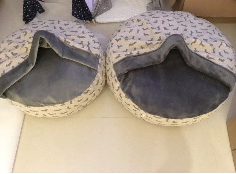 May include: Two round pet beds with a grey fleece lining and a beige outer fabric with a dachshund print.