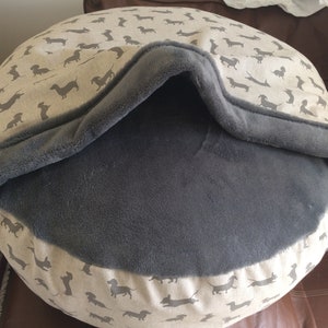 May include: A round, gray and beige dog bed with a removable, gray fleece cover. The bed has a dachshund print on the outer fabric.
