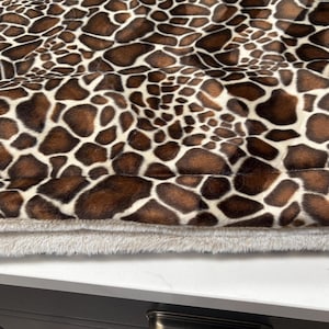 May include: Close-up of a pet bed with a giraffe print pattern in brown and white. The bed has a soft, plush, light gray bottom layer.
