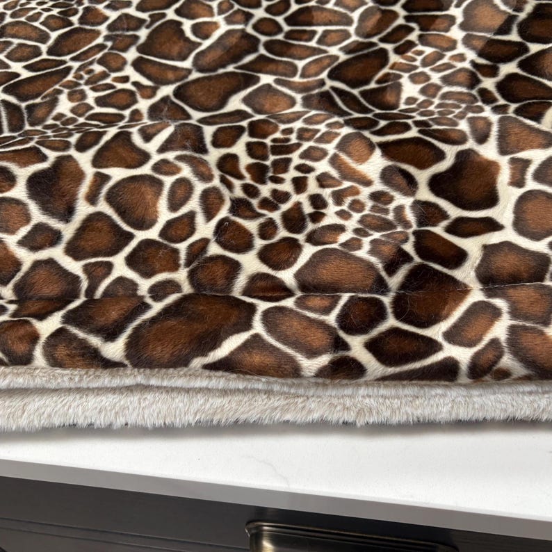 May include: Close-up of a pet bed with a giraffe print pattern in brown and white. The bed has a soft, plush, light gray bottom layer.