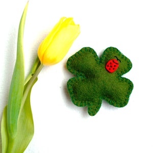 May include: A green felt four-leaf clover with a red ladybug sewn on it. A yellow tulip with green stem is in the background.