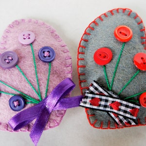 May include: Two felt heart ornaments with button embellishments. One heart is pink with purple buttons and a purple ribbon. The other heart is gray with red buttons and a black and white checkered ribbon.
