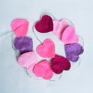 May include: A garland of felt hearts in pink, purple, and red, strung together with a silver wire.