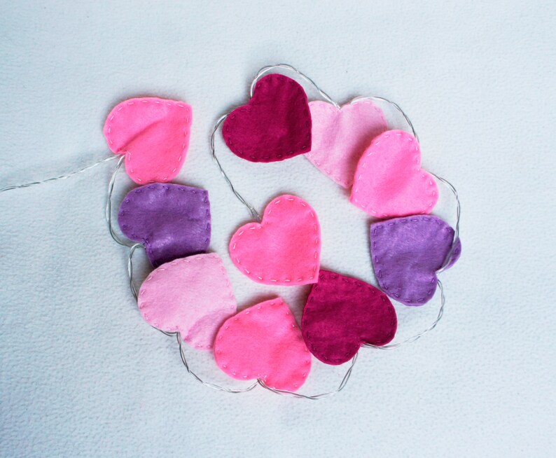 May include: A garland of felt hearts in pink, purple, and red, strung together with a silver wire.