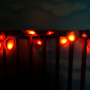 May include: A string of heart-shaped lights with warm, orange-red glow. The lights are strung across a wooden railing, creating a romantic and festive atmosphere.