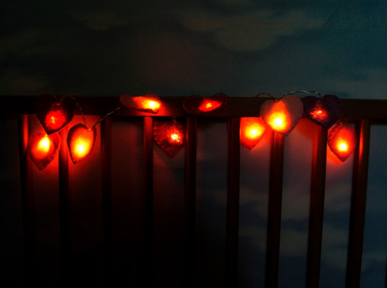 May include: A string of heart-shaped lights with warm, orange-red glow. The lights are strung across a wooden railing, creating a romantic and festive atmosphere.