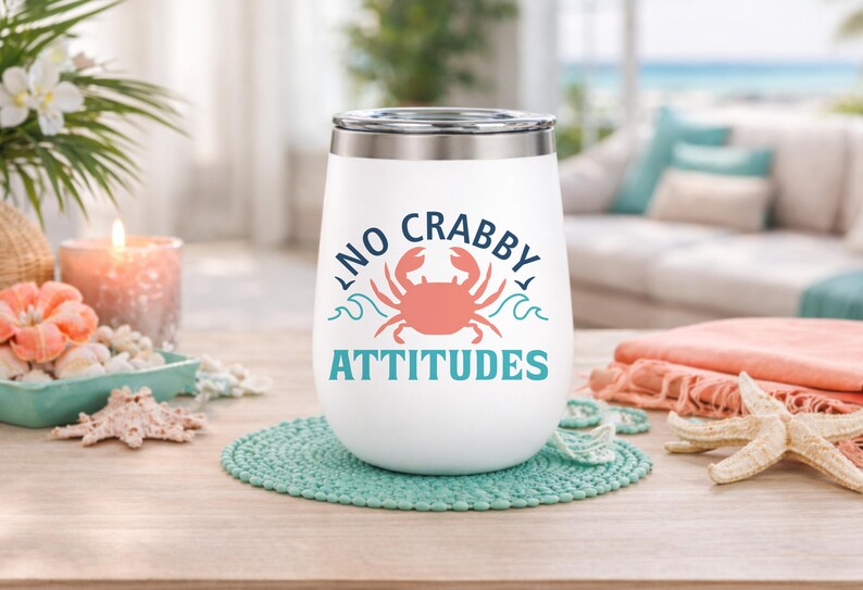 Puede incluir: Vaso de vino aislado blanco con tapa plateada, con el texto "NO CRABBY ATTITUDES" y un dise&ntilde;o de cangrejo coral. El vaso se encuentra sobre un posavasos turquesa, con decoraci&oacute;n de tem&aacute;tica playera en el fondo.