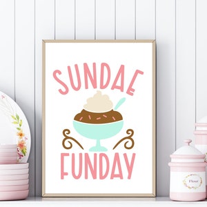 May include: A framed print with a pink background and the text "SUNDAE FUNDAY" in pink letters. A cartoon illustration of a sundae with chocolate sauce, whipped cream, and sprinkles is in the center of the print.