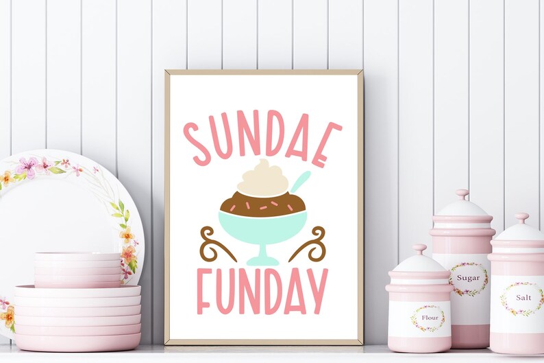 May include: A framed print with a pink background and the text "SUNDAE FUNDAY" in pink letters. A cartoon illustration of a sundae with chocolate sauce, whipped cream, and sprinkles is in the center of the print.