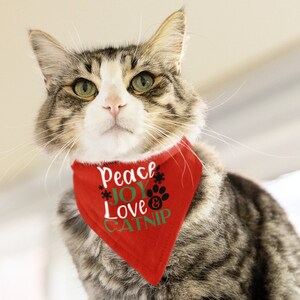 May include: A tabby cat wearing a red bandana with the text "Peace Joy Love & Catnip" in green and black lettering. The cat is looking directly at the camera.