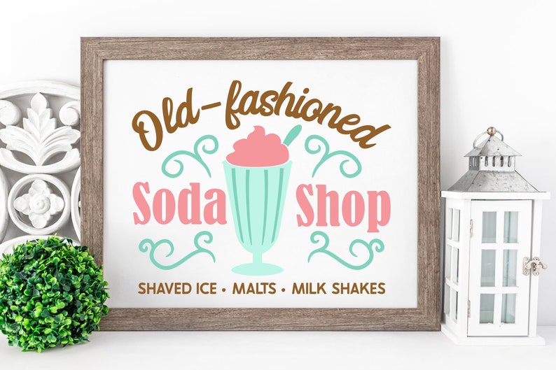 May include: A framed sign with the text "Old-fashioned Soda Shop" in brown, pink, and teal lettering. The sign also features a cartoon illustration of a milkshake with a cherry on top. The text "Shaved Ice - Malts - Milk Shakes" is printed below the illustration.