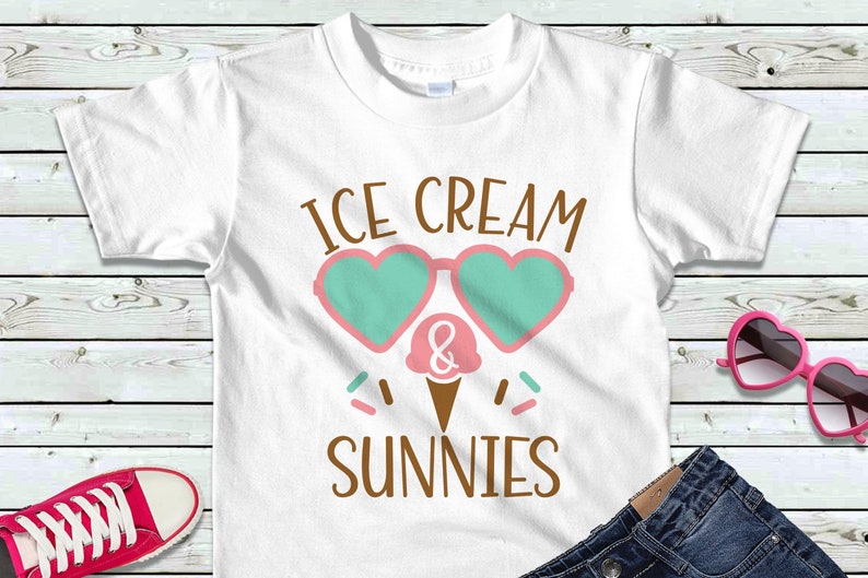 May include: White t-shirt with the text "ICE CREAM & SUNNIES" in brown letters. The text is surrounded by a pink and green heart-shaped sunglasses graphic and a pink and white ice cream cone graphic.