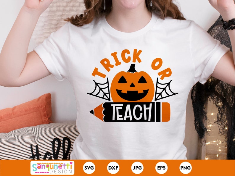 Pode incluir: Camiseta branca com o texto "Trick or Teach" em laranja e preto. Uma ab&oacute;bora preta e laranja com uma cara assustadora est&aacute; no centro do texto. Um l&aacute;pis preto e laranja com uma borracha vermelha est&aacute; abaixo do texto.