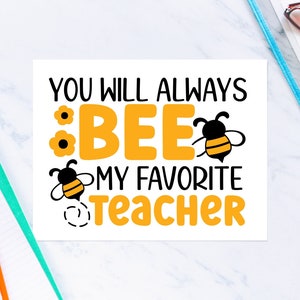 May include: A white square print with the text "YOU WILL ALWAYS BEE MY FAVORITE TEACHER" in black and orange. The word "BEE" is in large orange letters with bee and flower graphics. Stationery items surround the print.