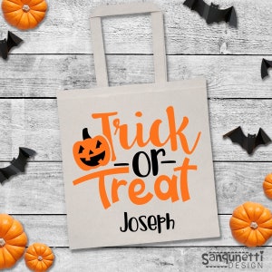 Puede incluir: Una bolsa de lona blanca con un dise&ntilde;o de "Truco o Trato" naranja y negro y una calabaza con una cara de calabaza. El nombre "Joseph" est&aacute; impreso en negro debajo del dise&ntilde;o.