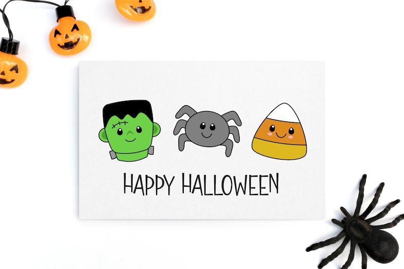 Pu&ograve; includere: Un biglietto bianco con un Frankenstein verde, un ragno grigio e un mais caramellato arancione e bianco con facce felici. Il testo "HAPPY HALLOWEEN" &egrave; sotto i personaggi.