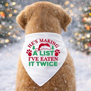 Op de afbeelding: Een hond draagt een witte kerstbandana met de tekst "He's making a list I've eaten it twice" in rood en groen. De hond bevindt zich in een besneeuwde buitenomgeving met vage kerstverlichting op de achtergrond.