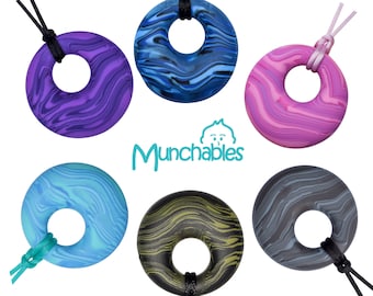 May include: Six colorful silicone teething necklaces with marbled patterns in blue, purple, pink, green, black, and gray. Each necklace has a round pendant with a hole in the center. The necklaces are all on a white background.  Munchbables.