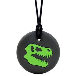 May include: A black necklace with a round, grey pendant featuring a green dinosaur skull silhouette.