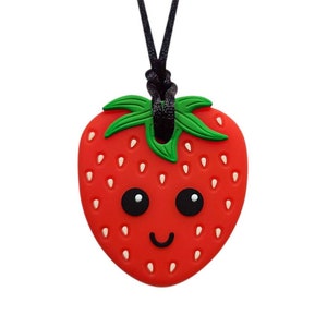 May include: A red silicone strawberry pendant with a green stem and a smiling face, hanging from a black cord.