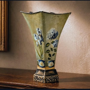 May include: A decorative vase with a flared shape, featuring painted floral designs of irises and hydrangeas in shades of blue and white. The vase has a textured, light green background and a detailed, dark brown base. It stands approximately 14 inches tall.