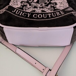 May include: A black and pink Juicy Couture crossbody bag. The bag features a pink and black design with the words "Juicy Couture" and a crest with two pink lions. The bag has a pink strap and a light pink bottom.