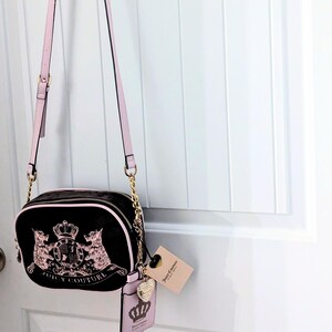 May include: Black crossbody bag with pink accents and gold-tone chain straps. The bag features a pink and gold emblem with the words "Juicy Couture". A matching pink cardholder and tag are attached.