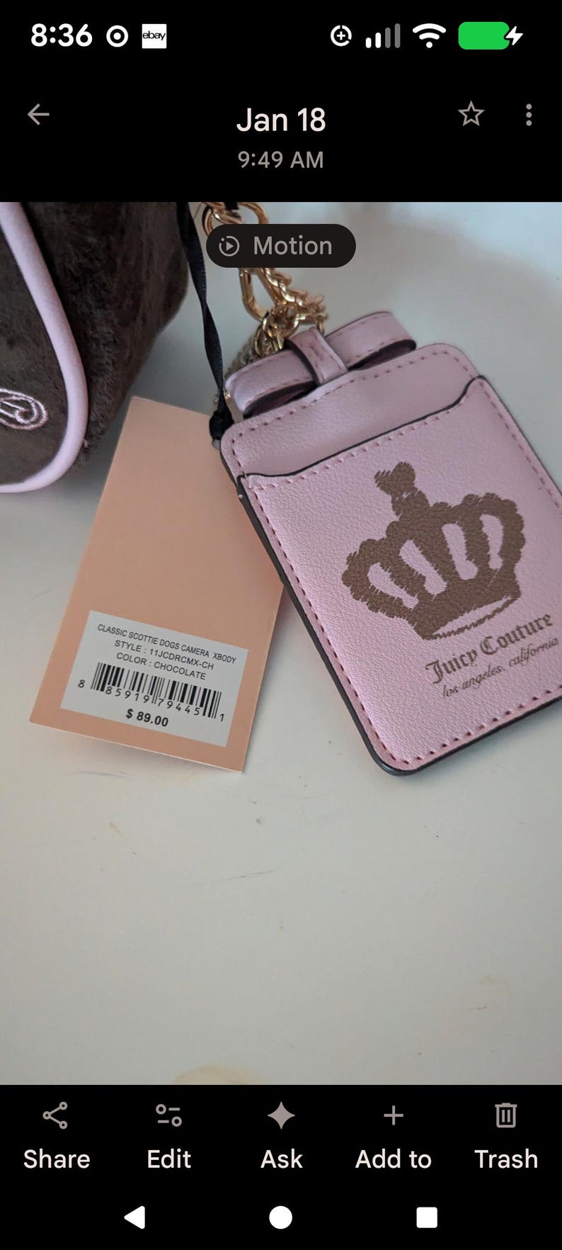 May include: A pink Juicy Couture cardholder with a gold-colored chain and bow detail. The cardholder features a crown design and the brand's logo. A tag with product information is also visible.